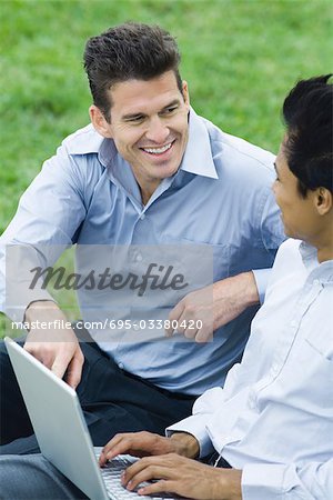 Zwei Männer sitzen im Park mit Laptop-Computer, Lächeln einander betrachten
