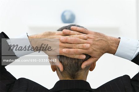 Business man with hands behind head looking at globe, rear view