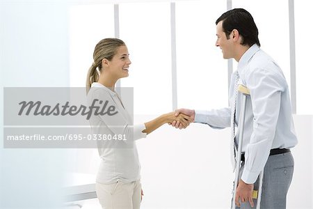 Man on crutches shaking woman's hand, side view