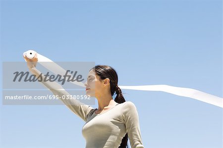 Woman holding up roll of paper outdoors, eyes closed, low angle view