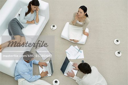 Team of professionals working together on floor, one woman napping on sofa, overhead view