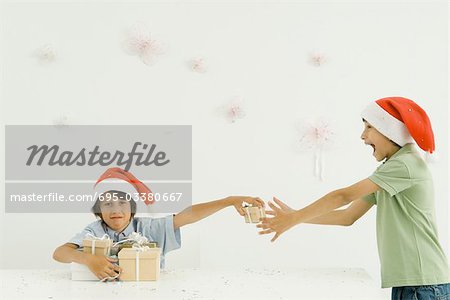 Two boys wearing Santa hats stacking presents, confetti falling around them