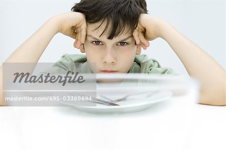 Boy sitting at table, holding head, glaring at camera