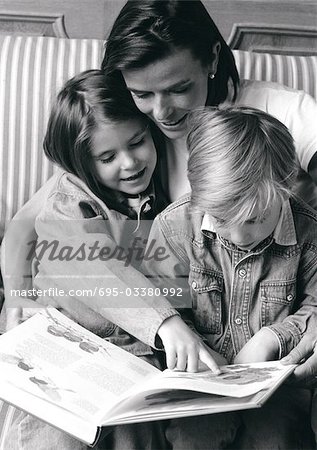 Jeune femme tenant deux enfants sur les genoux, regardant le livre, b&w