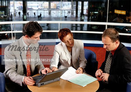 Three people sitting at table, one holding laptop computer