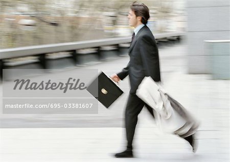 Businessman holding briefcase and overcoat, running, blurred