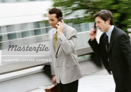 Two businessmen using cell phones outside, blurred