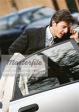 Kaufmann hinter der geöffneten Autotür mit Handy