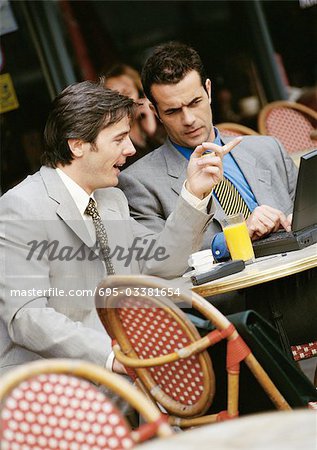 Two businessmen sitting at cafe terrace, looking at laptop computer