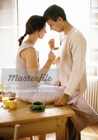 Femme et l'homme face à face, femme assise sur une table, tenant croissant