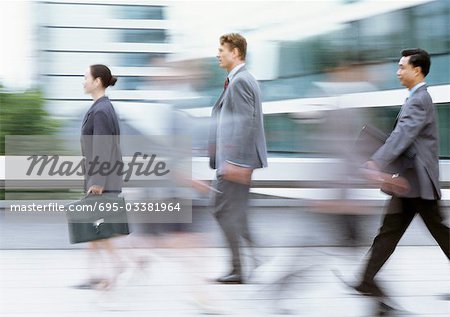 Three business people walking with briefcases, side view, blurred