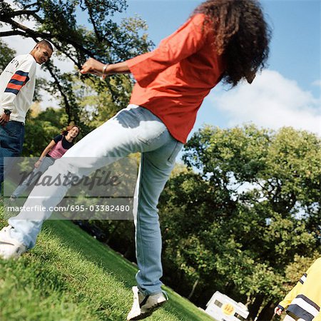 Young people together outside, young woman jumping in foreground, rear view