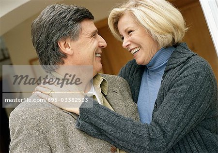 Homme et femme souriant face à face, femme avec bras autour de l'homme