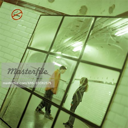 Young people talking together in subway station corridor, viewed in mirror.