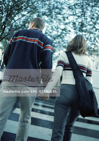 Young couple holding hands crossing on pedestrian crossing, rear view