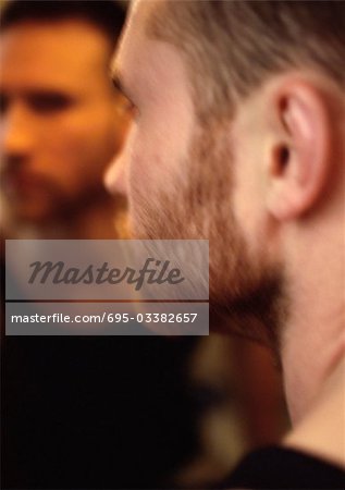 Man's face, view from over the shoulder, man's reflection in mirror in background