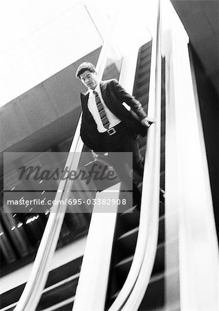 Businessman going down escalator, looking down, b&w.