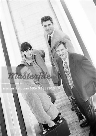 Group of business people on moving walkway, looking at camera, high angle view, b&w