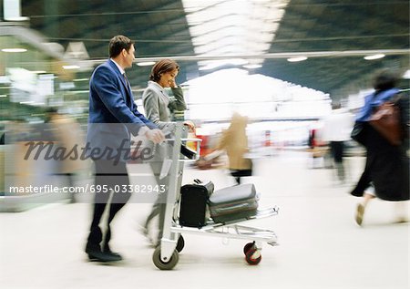 Businessman and businesswoman walking together with luggage through station, blurred.
