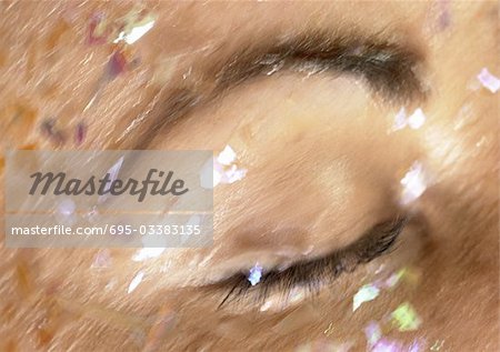 Woman's closed eye with glitter on face, close-up, blurry.