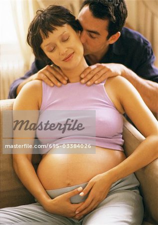 Man massaging pregnant woman's shoulders, kissing her neck