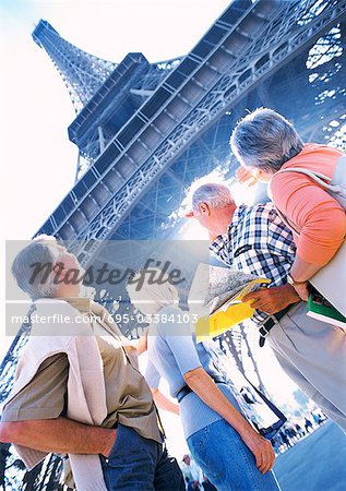 France, Paris, mature tourists looking up at Eiffel Tower, low angle view