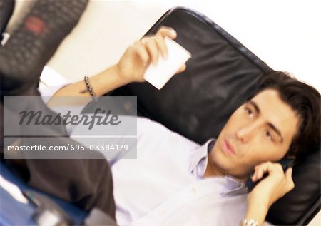 Man sitting with feet up, talking on telephone and holding plastic cup