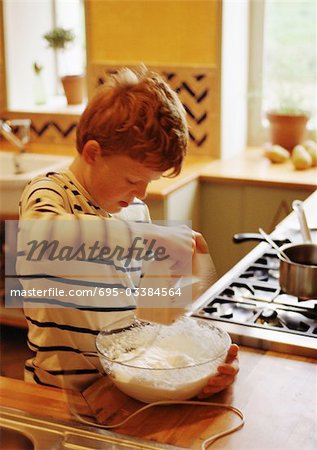 Child standing in kitchen, mixing batter with electric mixer, blurred motion
