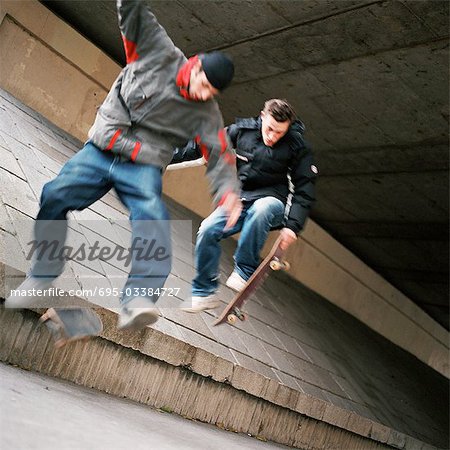 Young men in mid-air jump with skateboards, blurred