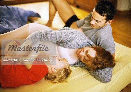 Paar mit Kind auf dem Bett liegend