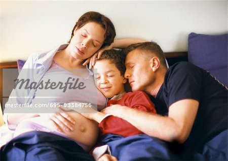 Schwangere Frau mit Mann und Kind im Bett sitzend