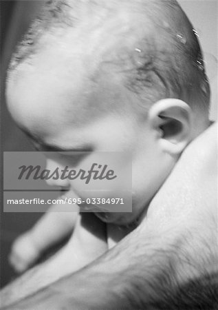 Baby with wet hair held in father's hands, close-up, b&w