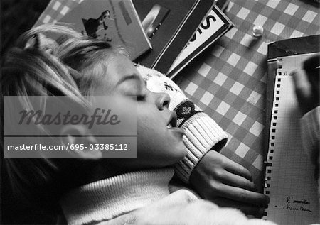 Girl resting head on arm writing, elevated view, b&w