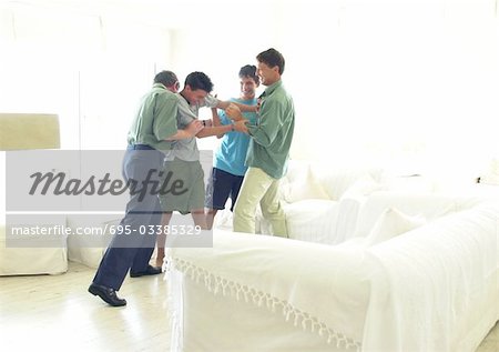 Großvater, Vater und Boys stehen im Wohnzimmer, playfighting