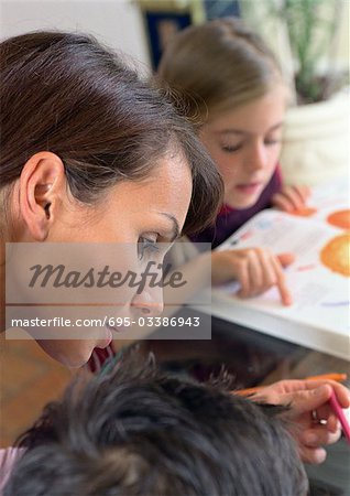 Mother working with child, daughter in background reading.