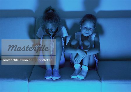 Deux petites filles, assis sur le canapé à regarder la télévision dans l'obscurité, rire