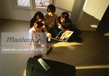 Young boys and girls sitting on floor looking at a book, high angle view