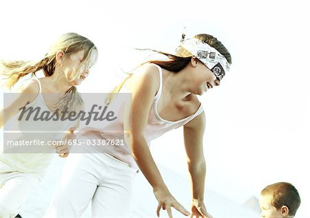 Blindfolded girl reaching and smiling outdoors, two children in background