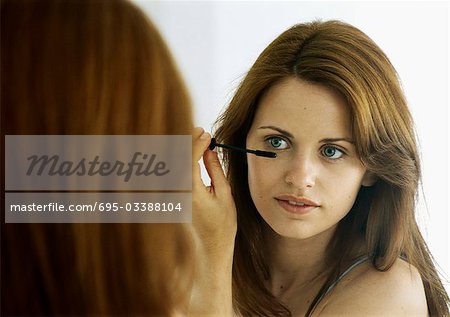 Young woman applying mascara in mirror