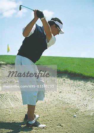 Golfer swinging in sand trap