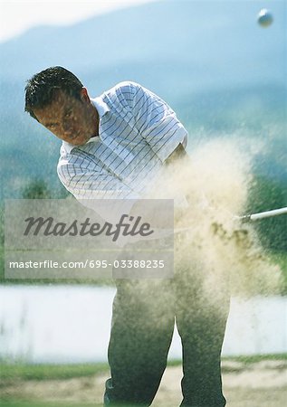 Golfer, mid-swing in sand trap, with sand in mid-air