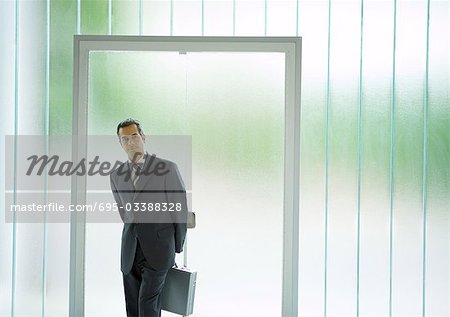 Businessman standing in front of door, holding briefcase behind back