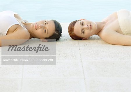 Two women lying on ground by edge of pool
