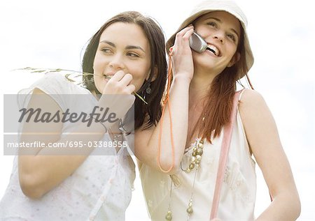 Two young woman outdoors, one using cell phone