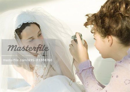 Preteen girl taking photo of friend dressed in wedding dress