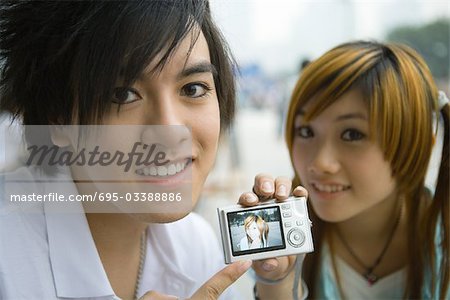 Teenage couple, man holding up digital camera showing photo of girlfriend