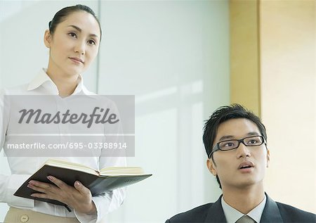 Business executive and woman holding agenda, both looking out of frame