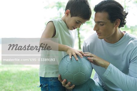 Boy looking at soccer ball with father