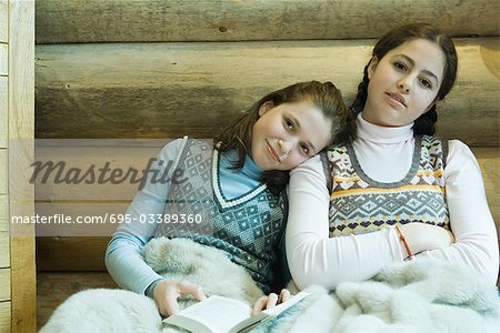 Couverture de deux adolescentes partage, souriant à la caméra, un tenant un livre, de se reposer la tête sur l'épaule de l'autre
