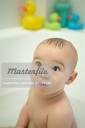 Naked baby sitting in bathtub, looking up, wide eyes